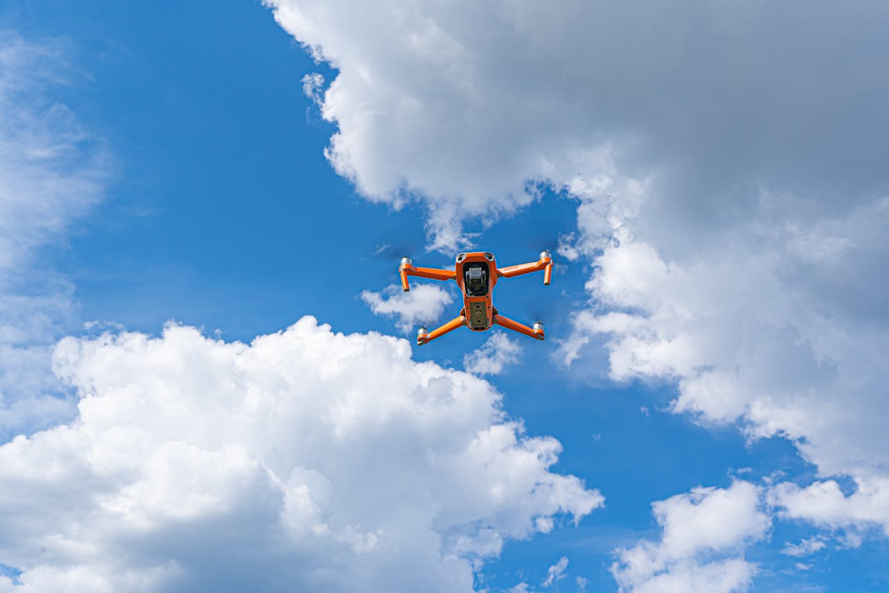 Orange drone flying against a dramatic cloudy sky, showcasing modern technology and aerial expertise.